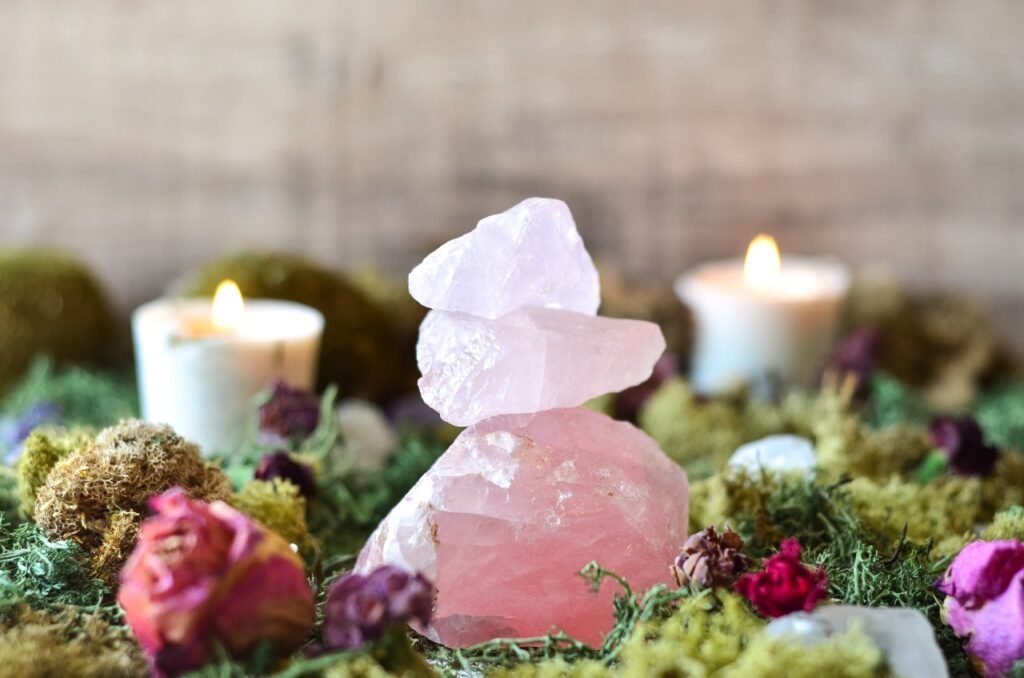 Três pedras de quartzo rosa empilhadas, elas estão em cima e cercadas por folhas e rosas secas.