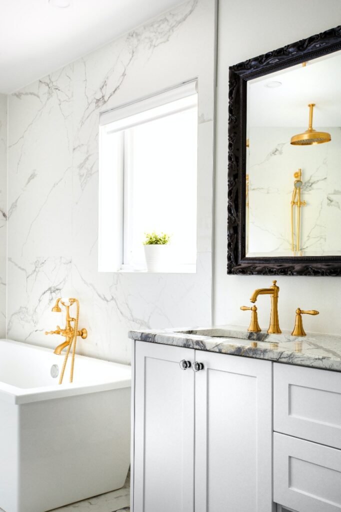 Banheiro de paredes e chão todo em mármore branco, com detalhes em dourado.