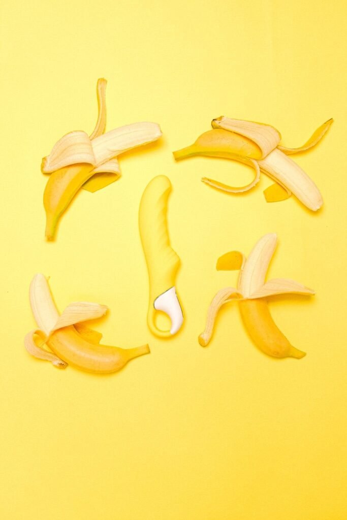 Vibrador de ponto G amarelo com a ponta levemente curvada, com quatro bananas em volta.