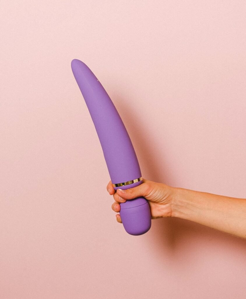 Mão de uma pessoa segurando um vibrador varinha mágica lilás. 