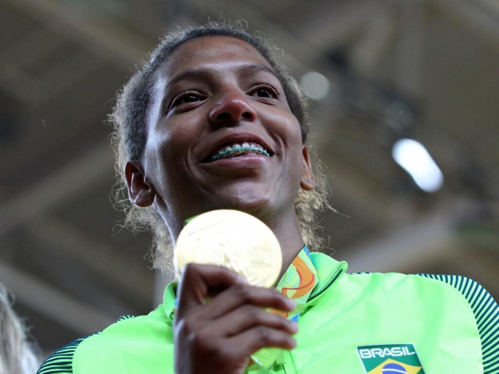Rafaela Silva com uniforme olímpico mostra sorriso segurando uma medalha de ouro.