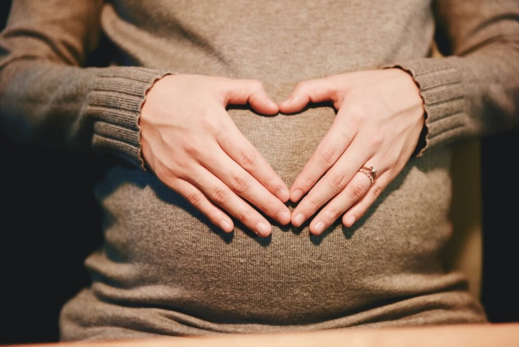 Mulher grávida fazendo coração com as mãos sobre a barriga.