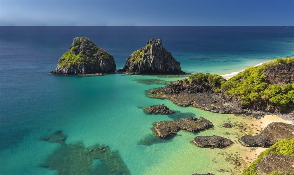 Praia de Fernando de Noronha, um dos destinos para lua de mel no Brasil, vista de cima, com o mar e algumas rochas.