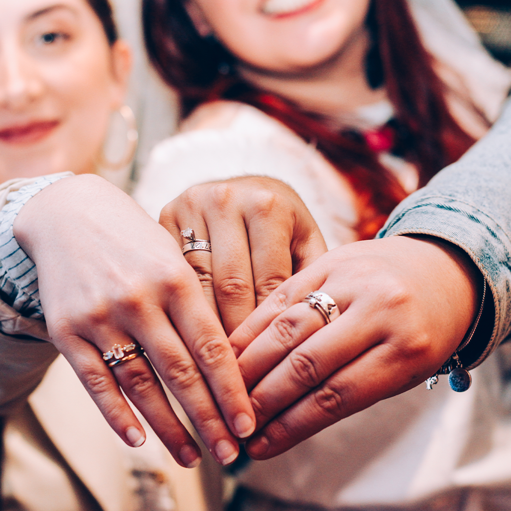 Três mulheres mostrando suas mãos com anéis nos dedos
