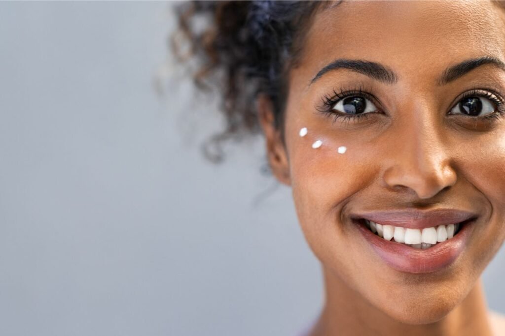 Mulher negra sorrindo com gotas de protetor solar abaixo de um dos olhos