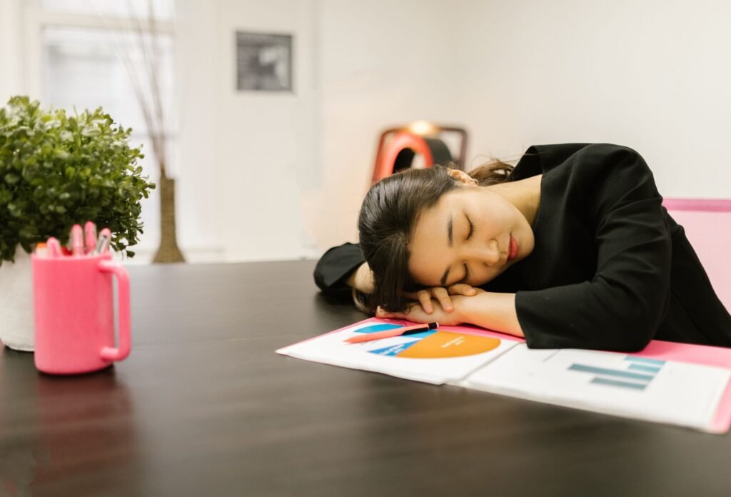 Mulher cochilando apoiada na mesa, em cima de papéis com gráficos do trabalho