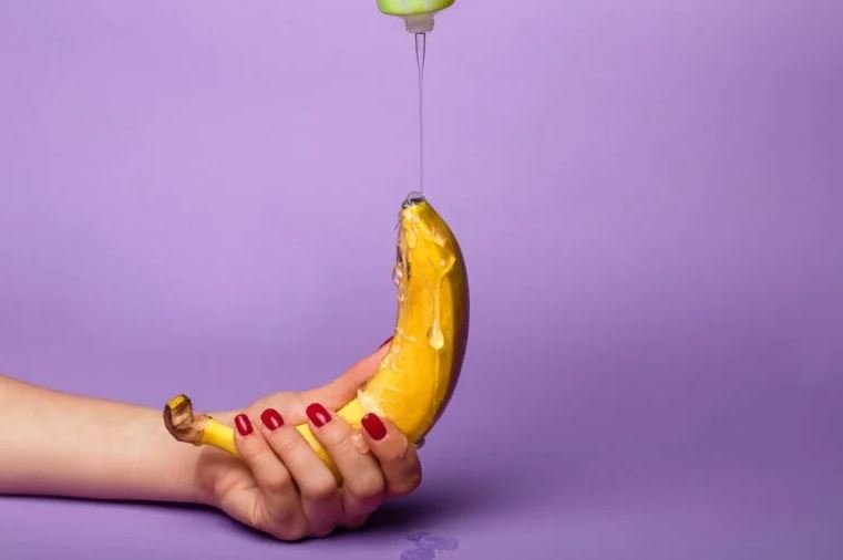 Mão de mulher segurando banana e derrubando lubirificante